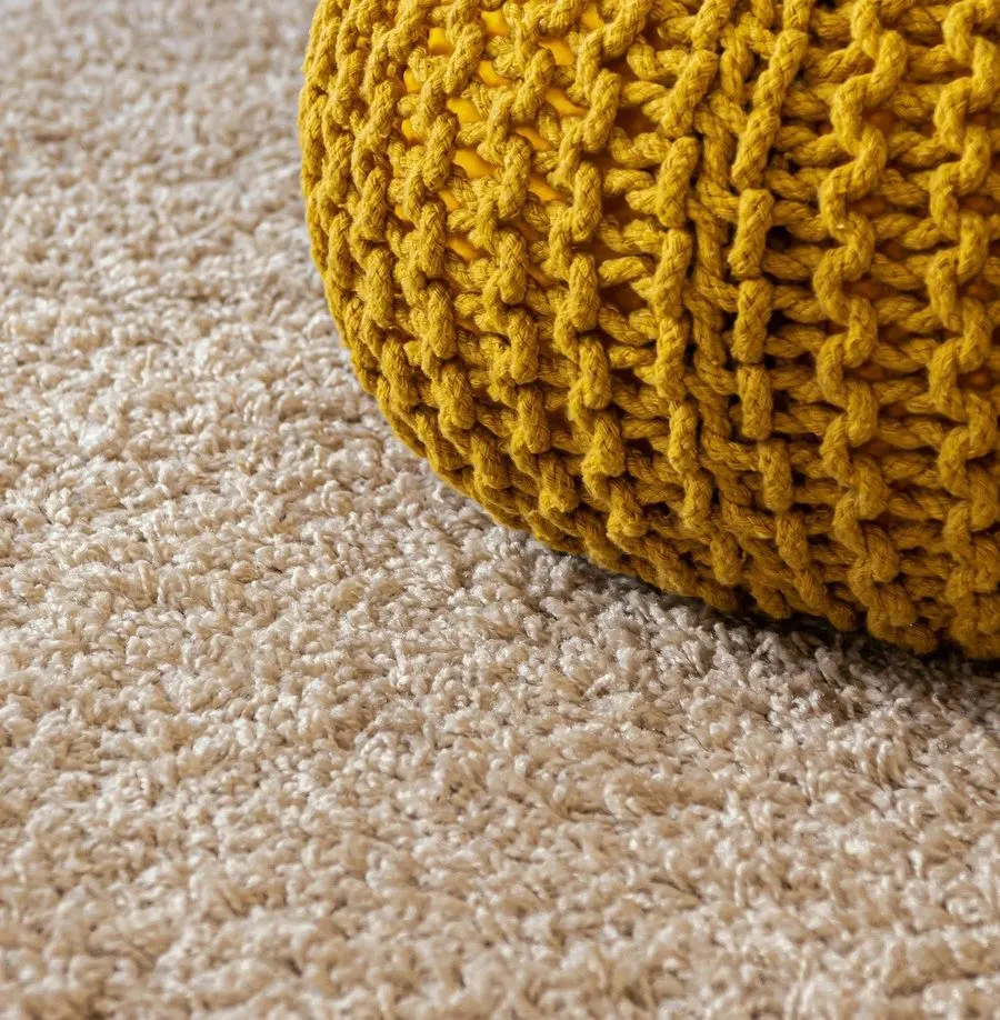 Close-up of soft beige carpet with a knitted pouf